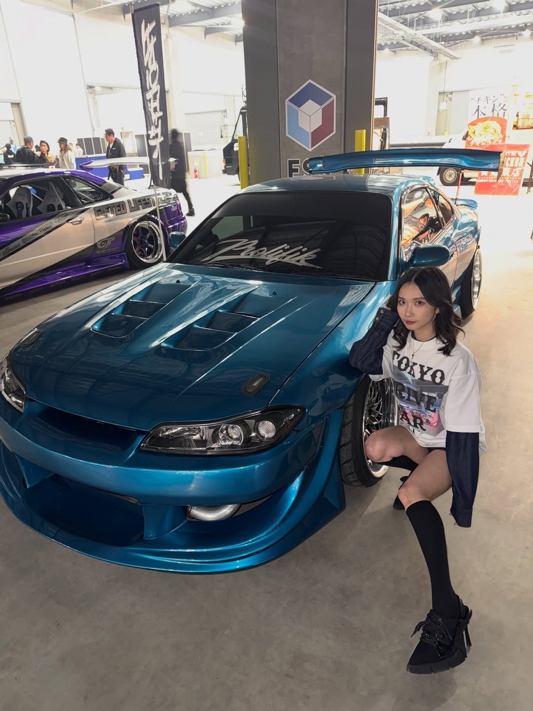 A model posing against the fender of a blue Nissan Silvia at the event